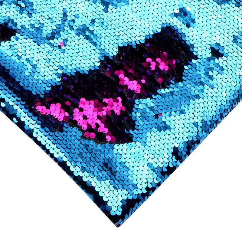 Un gros plan du Tissu pailleté bicolore réversible au mètre de Longan Craft France montre des paillettes bleues brossées pour révéler du rose et du noir, créant un effet saisissant de changement de couleur avec une finition brillante et réfléchissante, idéale pour les accessoires étincelants.