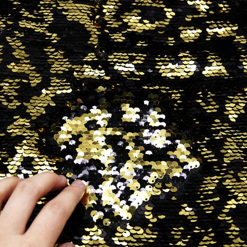 D'un geste de la main, le Tissu pailleté bicolore réversible au mètre de Longan Craft France passe du noir à l'or, mettant en valeur ses paillettes éblouissantes, parfaites pour créer des accessoires étincelants et des projets remarquables.