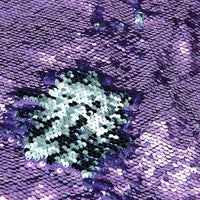 Gros plan sur le tissu pailleté bicolore réversible au mètre de Longan Craft France, dont les paillettes sont principalement violettes avec une section argentée au centre. Les paillettes denses de ce tissu à paillettes réversibles reflètent brillamment la lumière.