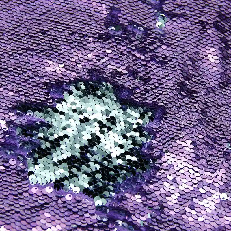 Gros plan sur le tissu pailleté bicolore réversible au mètre de Longan Craft France, dont les paillettes sont principalement violettes avec une section argentée au centre. Les paillettes denses de ce tissu à paillettes réversibles reflètent brillamment la lumière.