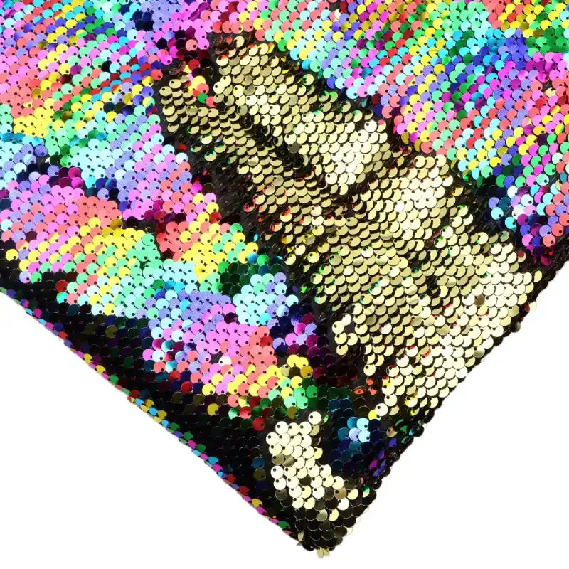 Gros plan sur un oreiller carré en tissu pailleté bicolore réversible au mètre de Longan Craft France, avec un pouce levé en paillettes dorées sur des paillettes réversibles multicolores.