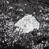 Un gros plan sur le Tissu pailleté bicolore réversible au mètre de Longan Craft France montre principalement des paillettes noires, avec une section brossée révélant l'argent brillant en dessous pour un effet chatoyant et texturé - parfait pour les accessoires.