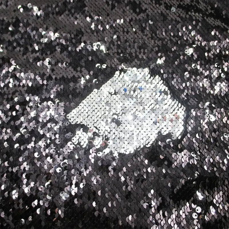 Un gros plan sur le Tissu pailleté bicolore réversible au mètre de Longan Craft France montre principalement des paillettes noires, avec une section brossée révélant l'argent brillant en dessous pour un effet chatoyant et texturé - parfait pour les accessoires.