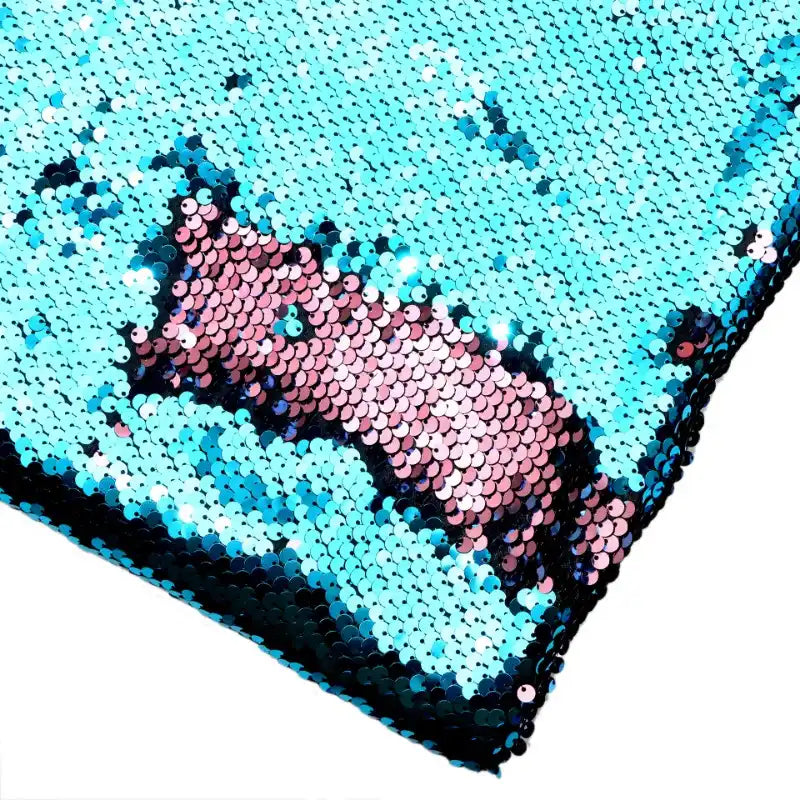 Un gros plan sur le Tissu pailleté bicolore réversible au mètre de Longan Craft France montre les paillettes bleues et roses qui scintillent lorsque la matière réversible crée des effets changeants lorsqu'elle est brossée dans des directions différentes.