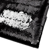 Un morceau plié du tissu pailleté bicolore réversible au mètre de Longan Craft France montre principalement des paillettes noires, avec une pièce argentée brossée créant un contraste audacieux sur le fond sombre.