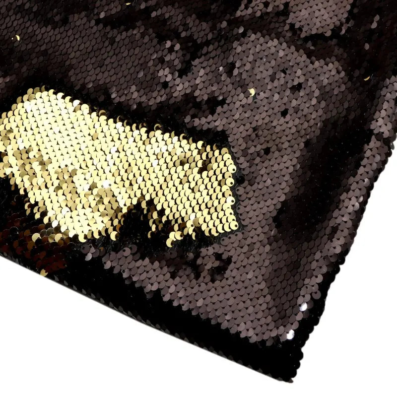 Un gros plan du tissu pailleté bicolore réversible au mètre de Longan Craft France montre principalement des paillettes noires, avec une section brossée révélant un dessous doré - une matière scintillante idéale pour les accessoires.