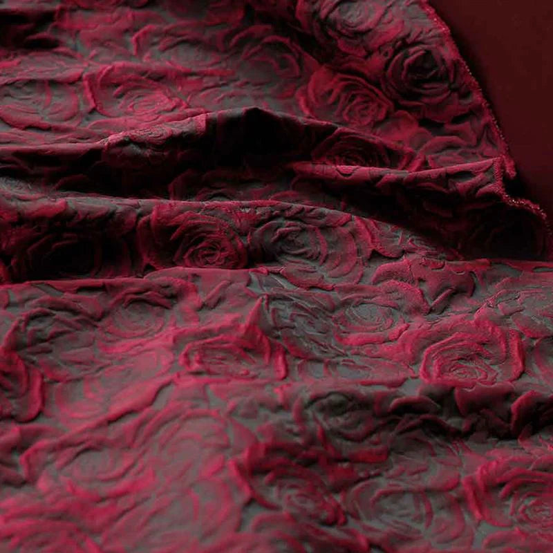 Gros plan sur le tissu brocart jacquard rose au mètre de Longan Craft France, qui présente un riche dégradé de rouge et de noir avec des motifs floraux en relief et d'élégants plis texturés.