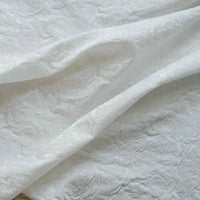 Tissu brocart jacquard rose au mètre de Longan Craft France, en tissu blanc embossé à motifs floraux, présente des roses en relief et un fini texturé raffiné dans de doux plis.