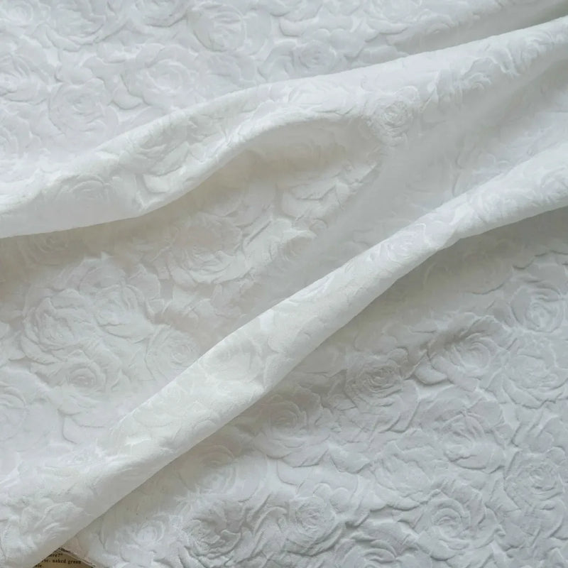Tissu brocart jacquard rose au mètre de Longan Craft France, en tissu blanc embossé à motifs floraux, présente des roses en relief et un fini texturé raffiné dans de doux plis.