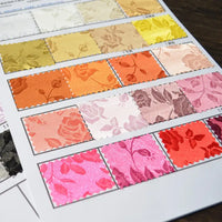 Une feuille de Longan Craft France Tissu satin jacquard rose au mètre à motifs floraux - jaune, pêche, orange, rose, rouge et beige - satiné textile pour la couture présenté sur une surface foncée.