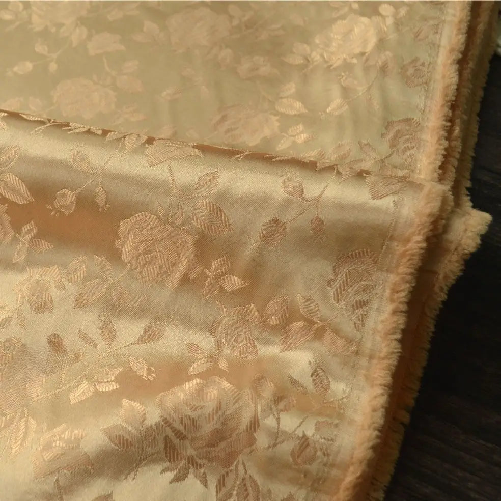 Gros plan sur le Tissu satin jacquard rose au mètre de Longan Craft France, un tissu floral en satin de couleur or avec des fleurs et des feuilles en relief, une brillance douce et un bord légèrement texturé, idéal pour la confection de robes.