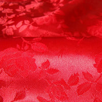 Gros plan sur le Tissu satin jacquard rose au mètre de Longan Craft France : un textile brillant à motifs floraux avec des roses et des feuilles en relief, parfait pour la couture. La finition satinée et les motifs complexes reflètent magnifiquement la lumière.