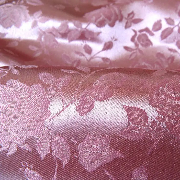 Gros plan sur le Tissu satin jacquard rose au mètre de Longan Craft France, un tissu de satin floral rose brillant parfait pour la couture. Les motifs gaufrés de roses et de feuilles se distinguent par leur texture et leur brillance visibles.