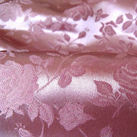 Gros plan sur le Tissu satin jacquard rose au mètre de Longan Craft France, un tissu de satin floral rose brillant parfait pour la couture. Les motifs gaufrés de roses et de feuilles se distinguent par leur texture et leur brillance visibles.