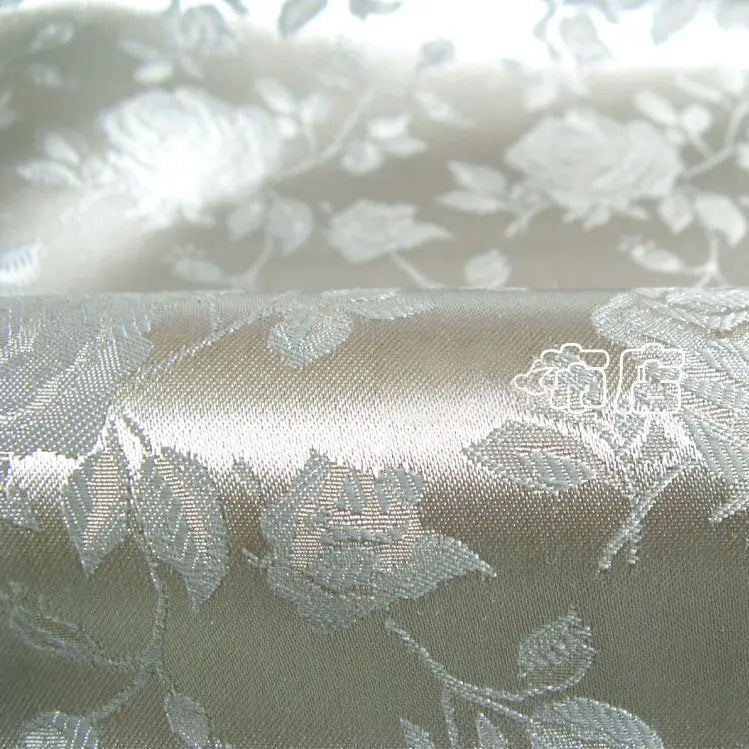 Gros plan sur le Tissu satin jacquard rose au mètre de Longan Craft France, un tissu satiné brillant à motifs floraux idéal pour la couture. Les roses et les feuilles tissées sont détaillées et brillantes, mettant en valeur sa texture luxueuse.