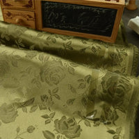 Gros plan sur le Tissu satin jacquard rose à motifs floraux de Longan Craft France, drapé sur une surface. À l'arrière-plan, une petite commode en bois avec tiroirs et section ardoise. Textile idéal pour confection de robes.