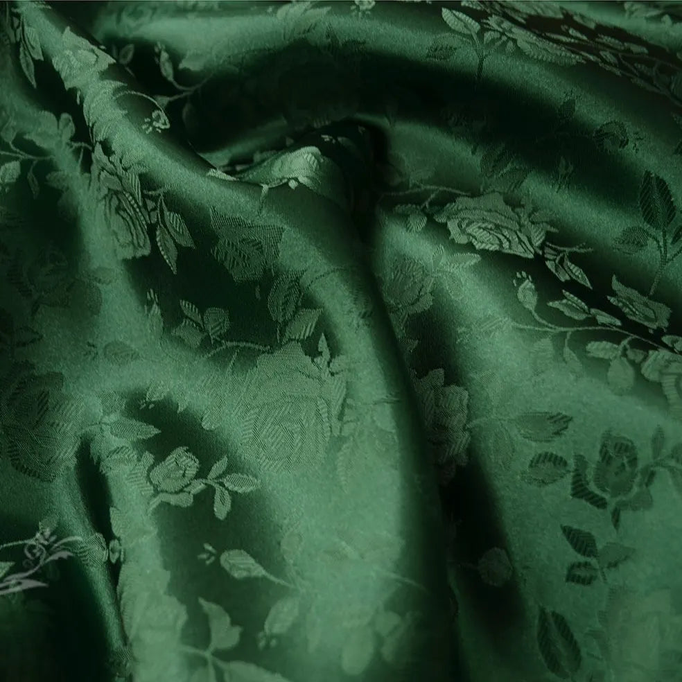 Gros plan sur le Tissu satin jacquard rose au mètre de Longan Craft France : satin vert foncé avec un motif floral complexe de roses et de feuilles, lisse et légèrement brillant - idéal pour la couture.