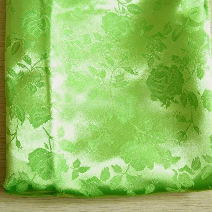 Un morceau plié du tissu satin jacquard rose au mètre de Longan Craft France, vert clair avec des motifs floraux gaufrés, repose sur une surface en bois - un textile satiné idéal pour la couture.