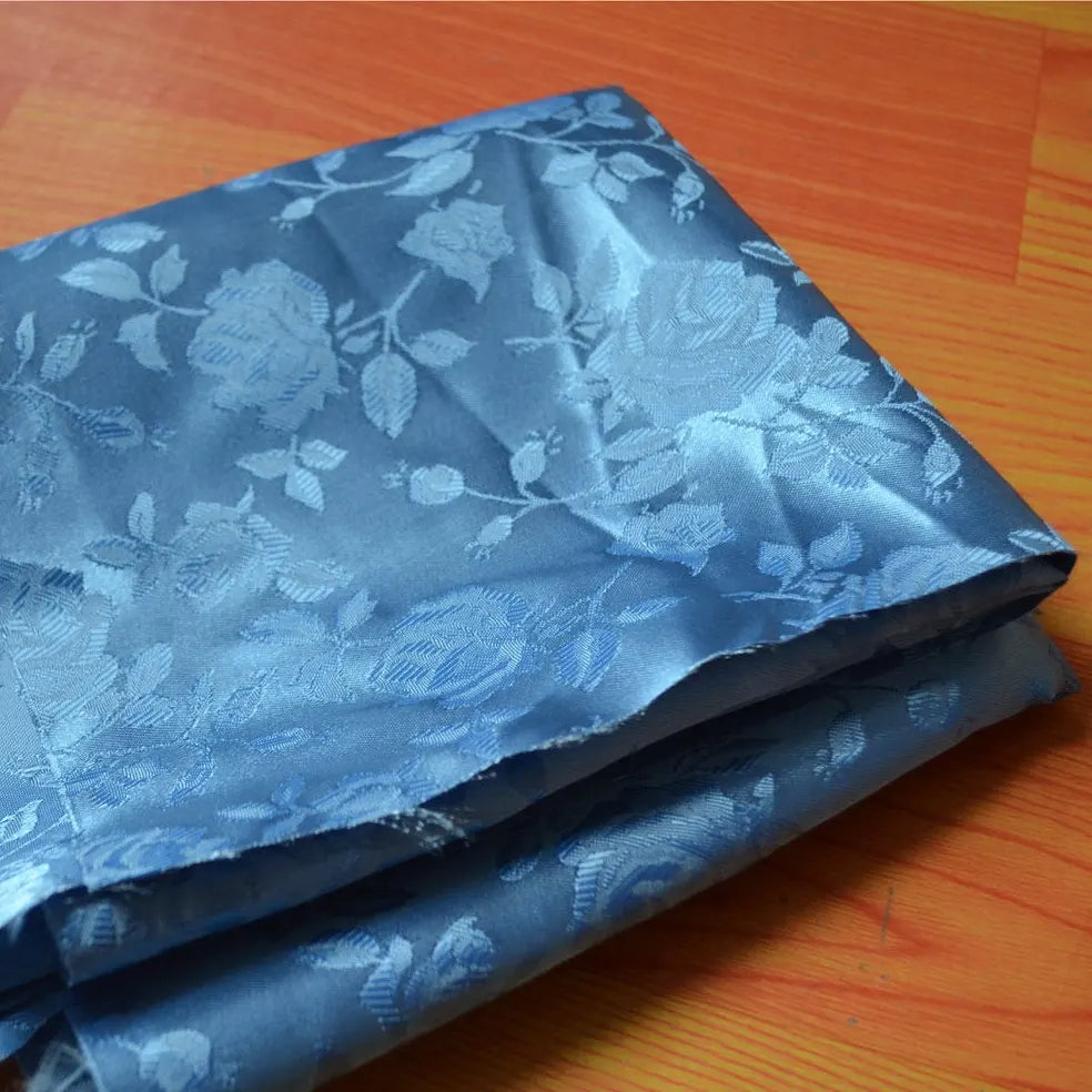 Un morceau de tissu satin jacquard rose à motifs floraux de Longan Craft France, vendu au mètre et idéal pour la confection de robes, est posé sur une surface en bois.