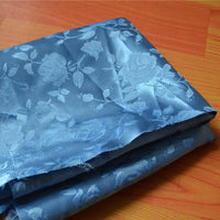 Un morceau de tissu satin jacquard rose à motifs floraux de Longan Craft France, vendu au mètre et idéal pour la confection de robes, est posé sur une surface en bois.