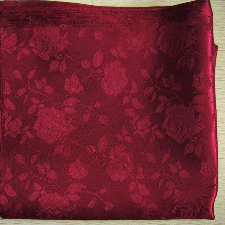 Une pièce de Longan Craft France Tissu satin jacquard rose au mètre, au subtil motif floral de roses et de feuilles, est présentée sur une surface en bois clair. Ce textile satiné est idéal pour la couture.