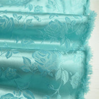 Gros plan sur le Tissu satin jacquard rose au mètre de Longan Craft France, un tissu de satin floral bleu turquoise avec une finition brillante et des motifs de roses tissés, présenté avec un léger effilochage sur un fond clair - idéal pour la couture.