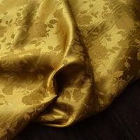 Le Tissu satin jacquard rose au mètre de Longan Craft France, un textile de satin brillant à motifs floraux pour la couture, est élégamment drapé sur une surface en bois sombre.