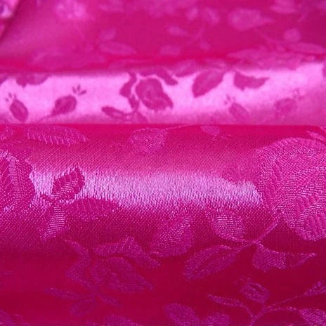 Gros plan sur le Tissu satin jacquard rose de Longan Craft France, qui présente un motif floral brillant avec des roses et des feuilles gaufrées d'un rose plus foncé - idéal pour la couture. Disponible au mètre.
