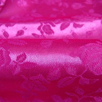 Gros plan sur le Tissu satin jacquard rose de Longan Craft France, qui présente un motif floral brillant avec des roses et des feuilles gaufrées d'un rose plus foncé - idéal pour la couture. Disponible au mètre.