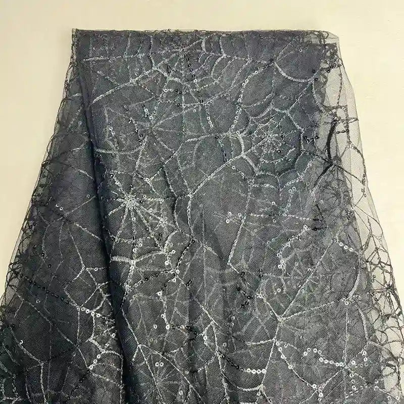 Le Tissu en tulle brodé de sequins au mètre de Longan Craft France présente un motif de toile d'araignée en paillettes argentées sur du tulle noir - idéal pour des décors et des costumes d'Halloween étincelants.
