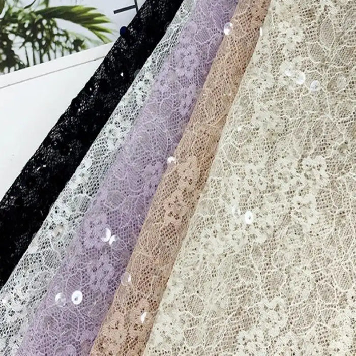 Cinq feuilles de Tissu dentelle à sequins au mètre de Longan Craft France en noir, blanc, lavande, beige et crème sont disposées côte à côte. La dentelle florale non extensible brille de mille feux - parfaite pour les robes de mariée ou le tissu dentelle mariage.