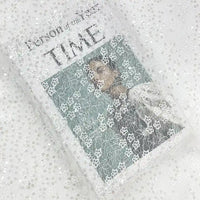 Un magazine Time intitulé "Person of the Year" est partiellement drapé de Tissu dentelle à sequins au mètre de Longan Craft France, une dentelle brodée ajourée non extensible idéale pour vêtements et robes de mariée.