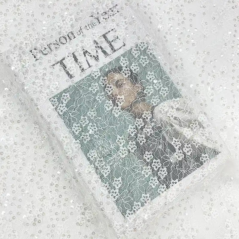 Un magazine Time intitulé "Person of the Year" est partiellement drapé de Tissu dentelle à sequins au mètre de Longan Craft France, une dentelle brodée ajourée non extensible idéale pour vêtements et robes de mariée.