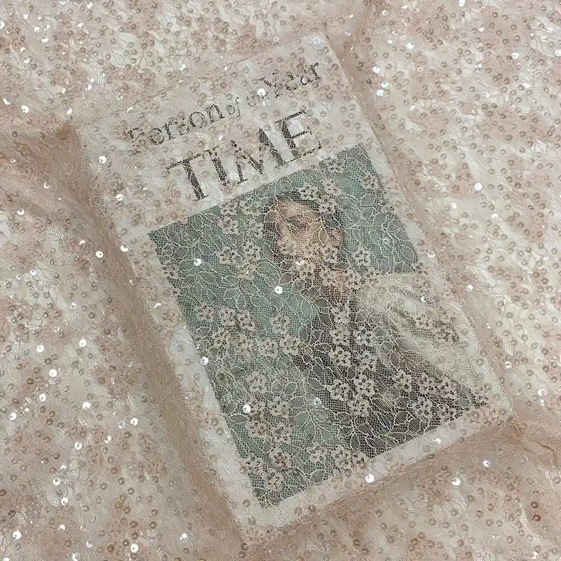Un livre intitulé "Tomorrow, and Tomorrow, and Tomorrow" repose sur le Tissu dentelle à sequins au mètre de Longan Craft France, une dentelle brodée élégante et non extensible, parfaite pour inspirer des idées de robes de chambre ou de robes de mariée.