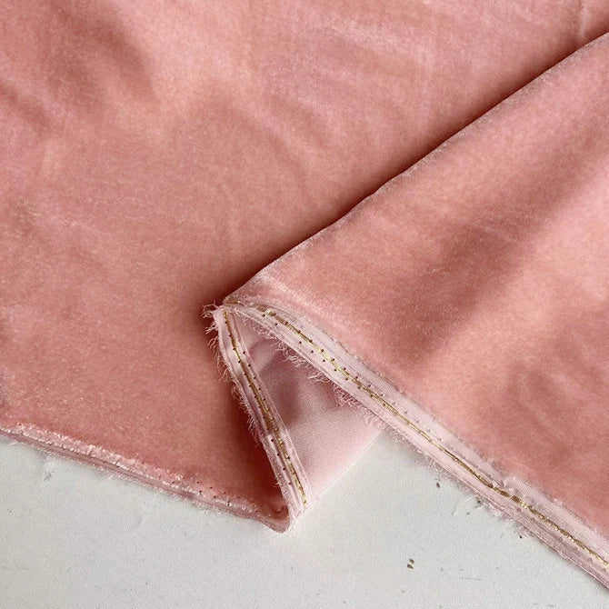 Un gros plan du Tissu velours de soie de mûrier doux au mètre de Longan Craft France montre un tissu rose clair aux bords non finis, un coin plié pour révéler les coutures et le dessous, reposant sur une surface pâle.
