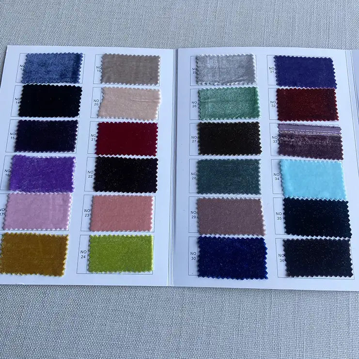 Un livre d'échantillons ouvert sur une surface grise texturée présente 20 échantillons de tissus, dont le luxueux Tissu velours de soie au mètre de Longan Craft France, un doux velours de soie de mûrier destiné aux peignoirs, à la couture, à l'artisanat et à l'ameublement.