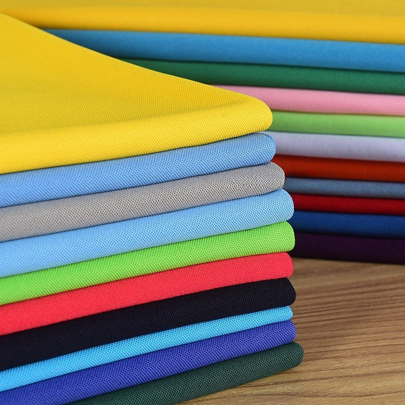 Une pile de Tissu piqué uni simple face au mètre de Longan Craft France, en jaune, vert, rouge, bleu, gris et noir, en maille piqué fine d'été pour les chemises à manches courtes DIY, soigneusement disposée sur une surface en bois.