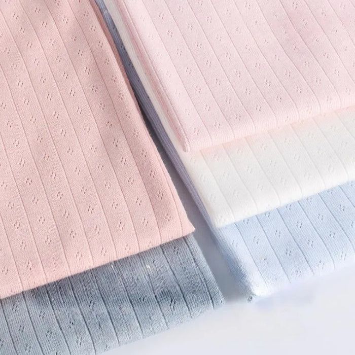 Quatre pièces de tissu jersey pointelle coton simple face de Longan Craft France, idéal pour confectionner des bodys et des pyjamas pour bébé, sont présentées dans des coloris rose pastel, blanc, bleu clair et gris avec de petits motifs d'œillets.