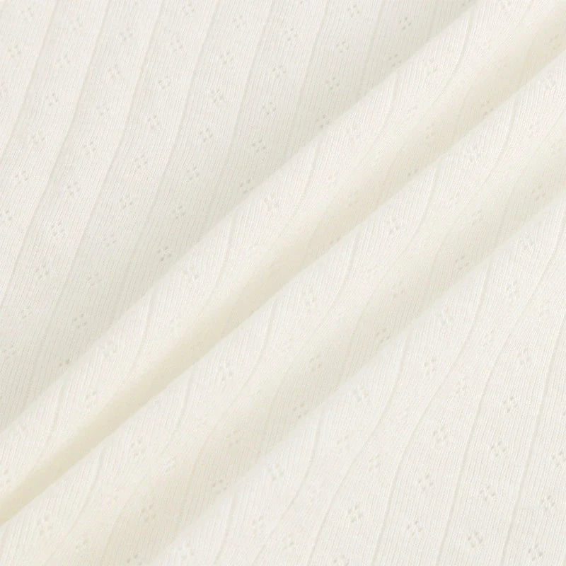 Gros plan sur le Tissu jersey pointelle coton simple face de Longan Craft France, de couleur crème, qui présente une maille côtelée à la texture ondulée et des trous décoratifs en diagonale. Les plis souples soulignent l'épaisseur du tissu, idéal pour les bodys et les pyjamas de bébé.