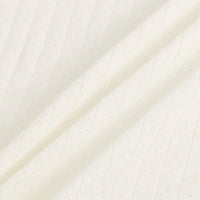 Gros plan sur le Tissu jersey pointelle coton simple face de Longan Craft France, de couleur crème, qui présente une maille côtelée à la texture ondulée et des trous décoratifs en diagonale. Les plis souples soulignent l'épaisseur du tissu, idéal pour les bodys et les pyjamas de bébé.