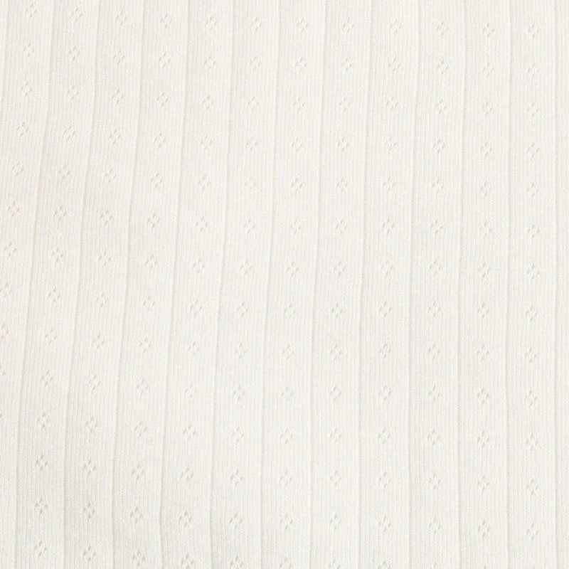 Gros plan sur le Tissu jersey pointelle coton simple face de Longan Craft France, un tissu en tricot de coton côtelé de couleur crème ou blanc cassé avec de petits détails texturés en forme de losange, idéal pour confectionner des bodys et des pyjamas pour bébés.