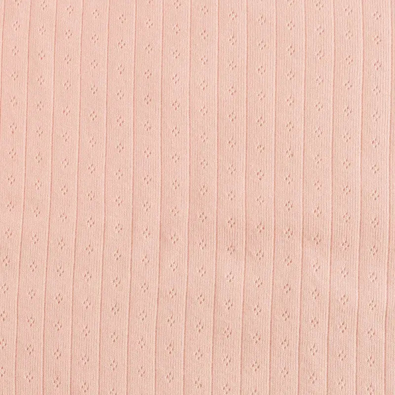 Gros plan sur le Tissu jersey pointelle coton simple face au mètre de Longan Craft France : tissu rose pâle, doux et lisse avec de petits oeillets verticaux - idéal pour le body DIY ou le pyjama bébé et les projets délicats.