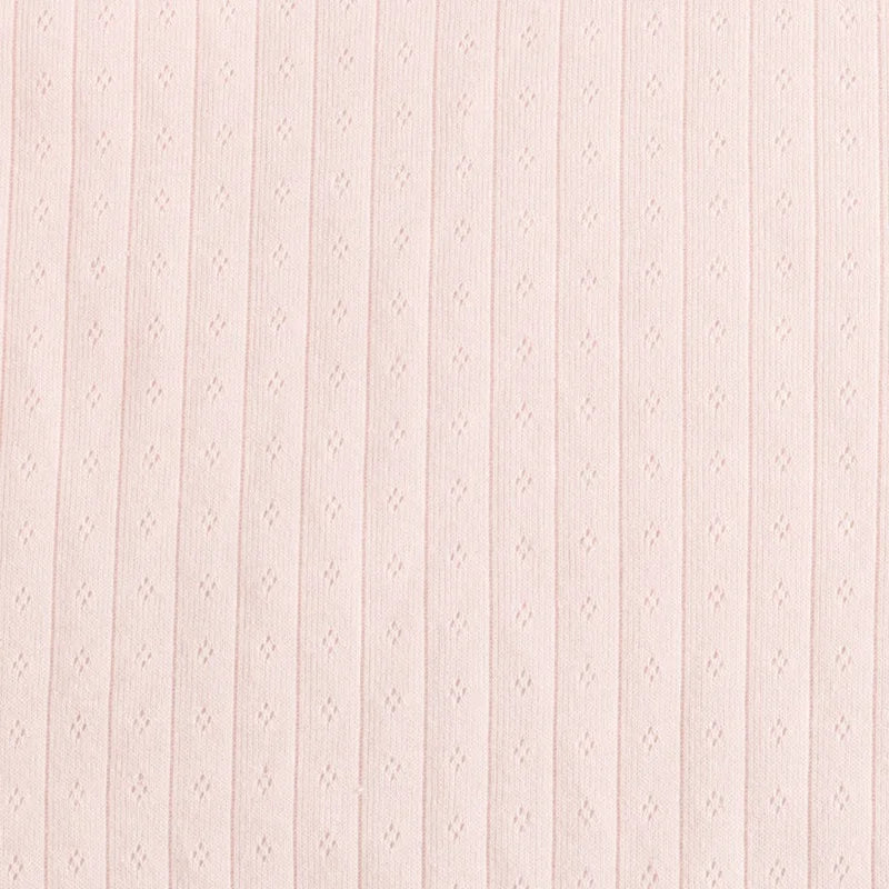 Gros plan sur la pointelle en jersey de coton rose pâle de Longan Craft France, qui présente des rayures verticales côtelées et des œillets en losange régulièrement espacés. Elle est idéale pour les bodys ou les pyjamas de bébé. Disponible au mètre.
