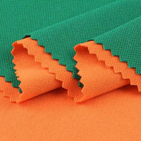 Deux pièces de Longan Craft France Tissu piqué motif œil d'oiseau à fil simple, vert et orange, sont superposées avec des bords en zigzag. Le tissu respirant est plié pour mettre en valeur les deux couleurs et sa texture œil d'oiseau, idéale pour les polos et les t-shirts d'été DIY.