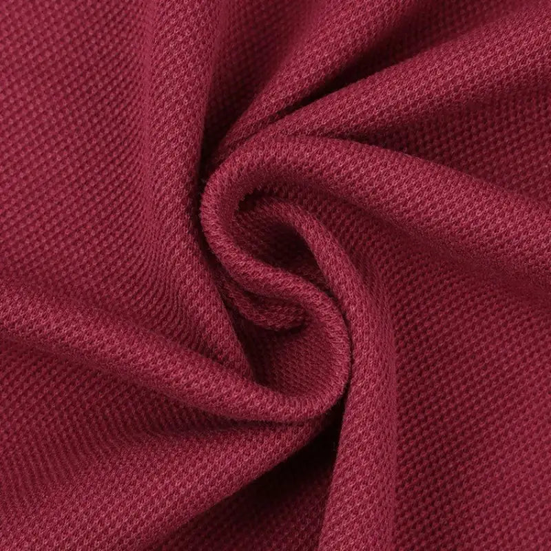 Gros plan sur le tissu piqué motif œil d'oiseau à fil simple de Longan Craft France, un tissu respirant et texturé de couleur rouge foncé, disposé en spirale pour montrer sa trame - idéal pour les polos et T-shirts d'été DIY.