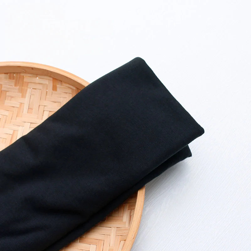 Un morceau de jersey multicolore en polyester et coton de Longan Craft France, idéal pour une tenue décontractée, est présenté sur un plateau rond en bambou tressé sur fond blanc.