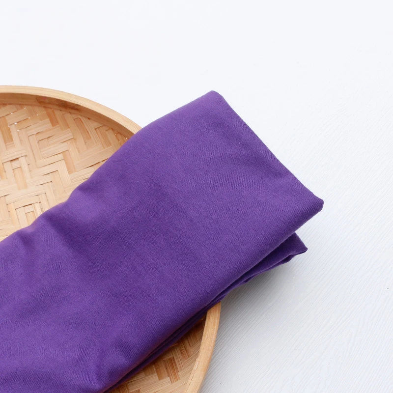 Un morceau de "Tissu en jersey simple au mètre" de Longan Craft France, polyester-coton multicolore, est plié sur un plateau rond en bambou sur un fond clair - idéal pour confectionner des vêtements décontractés.