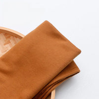 A piece of Longan Craft France Tissu en jersey simple au mètre, un jersey polyester-coton multicolore pour vêtements décontractés, est posé sur un plateau en bois tressé sur fond blanc.