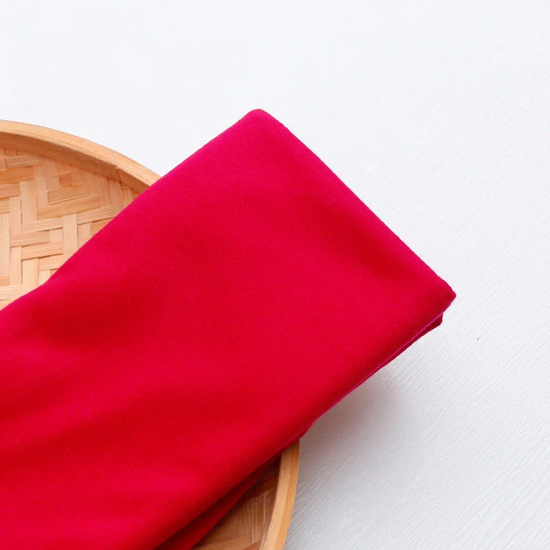 Un morceau plié du tissu jersey multicolore en polyester-coton de Longan Craft France pour vêtements de loisirs repose sur le bord d'un panier rond tressé, posé sur une surface blanche.