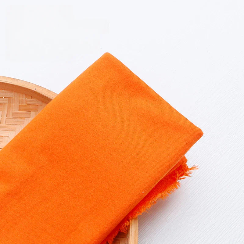 Un morceau de jersey multicolore en polyester et coton de Longan Craft France, idéal pour une tenue décontractée, est soigneusement plié avec des bords effilochés sur un plateau rond tissé sur un fond blanc.